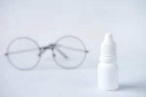 Eye drops on a surface in front of round glasses frames