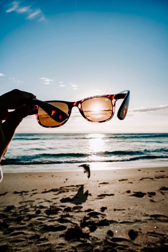 hand holding sunglasses over the sun on a beach