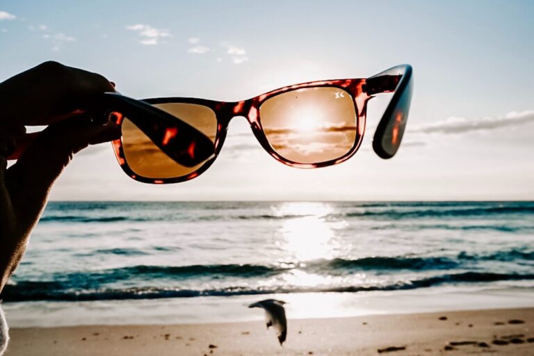 hand holding sunglasses over the sun on a beach