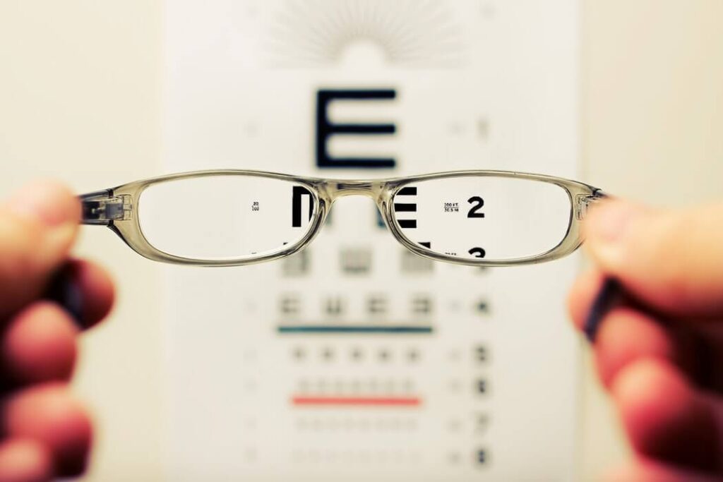Blurred hands holding glasses up to an optician's eye test chart.