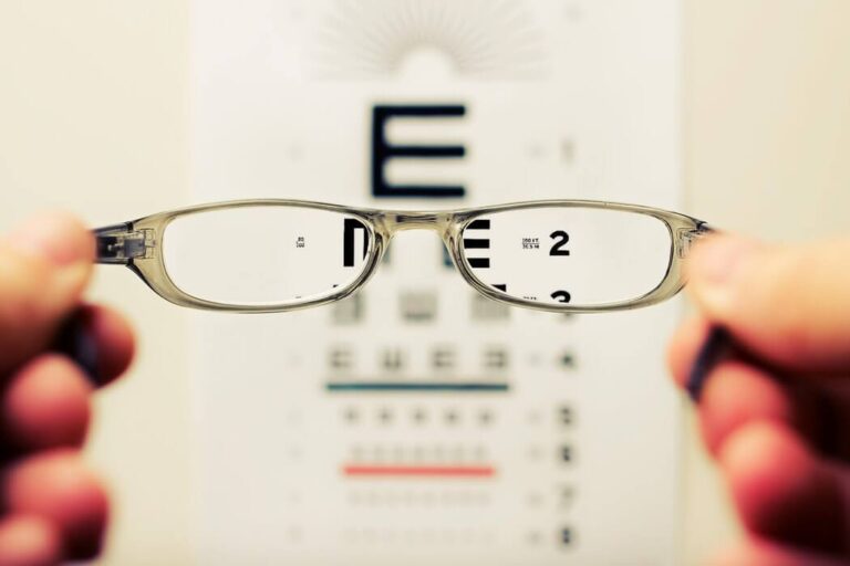 Blurred hands holding glasses up to an optician's eye test chart.