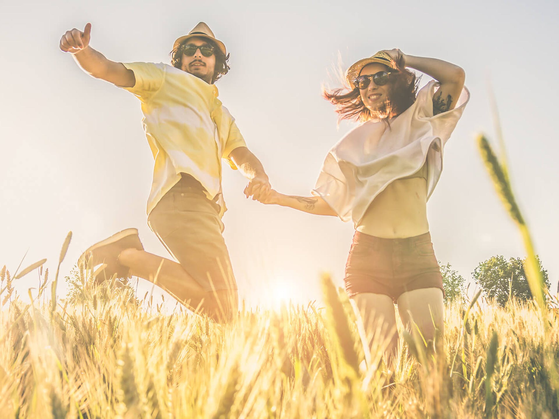Couple wearing hats and sunglasses jumping up in a sunny wheat field