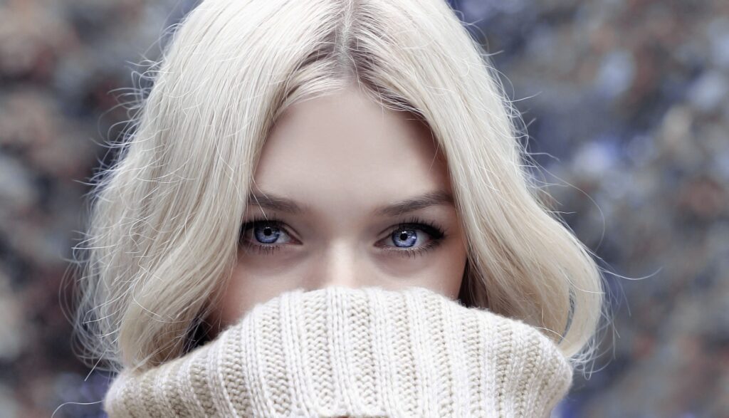 Blonde woman with blue eyes wearing a cream roll neck jumper