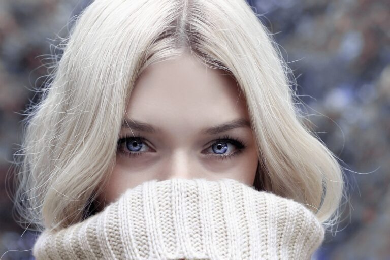 Blonde woman with blue eyes wearing a cream roll neck jumper