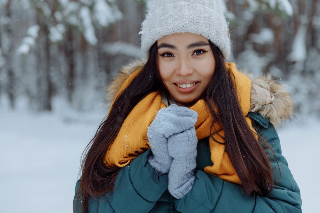 Brunette woman in hat, gloves and scarf smiling at the camera as she stands in the snow