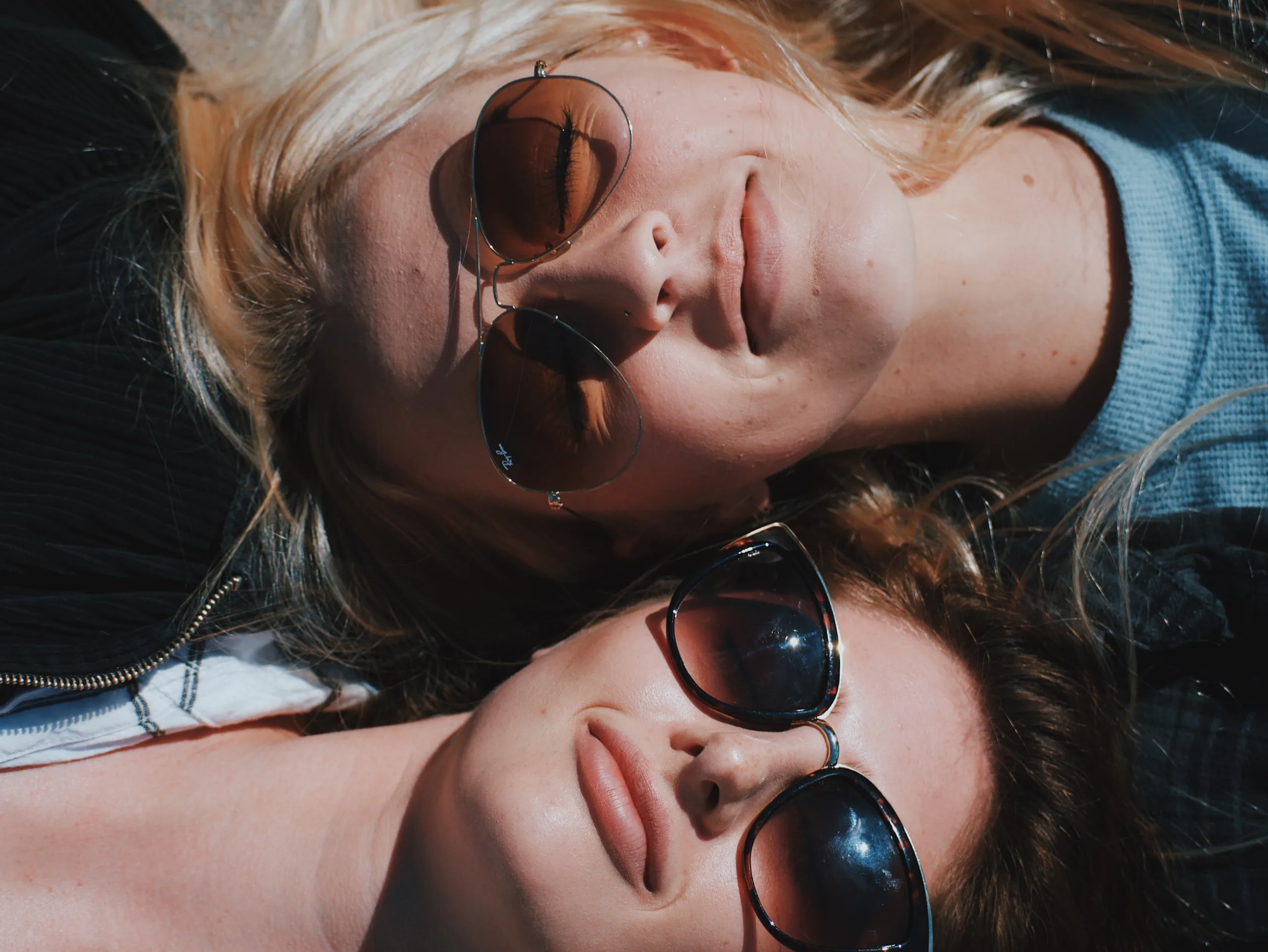 Two women lying head to head whilst wearing sunglasses