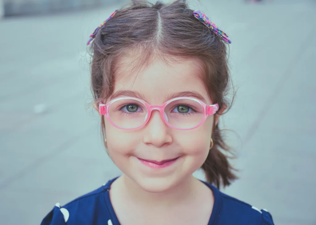 Brunette girl with pink glasses smiling at the camera