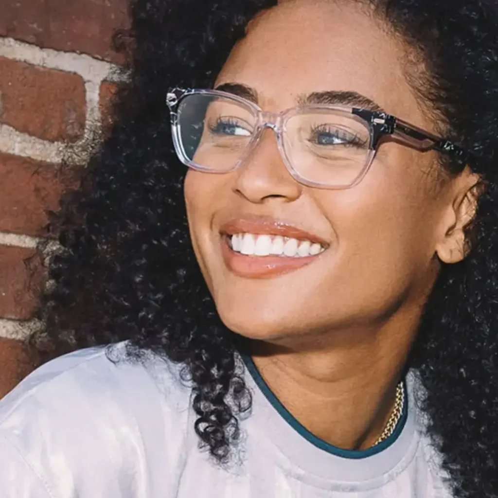 Woman smiling against a brick wall wearing Nike glasses